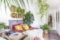 Bohemian bedroom with hanging plants, woven wall baskets, colorful pillows, and a record player on a wooden table.