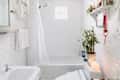 Bright bathroom featuring a white tub, shower curtain, potted plants, and decorative shelf with items.