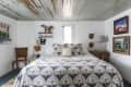 Cozy bedroom with patterned bedding, rustic wood ceiling, wall art, and decorative masks above the bed.