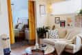 Cozy living room with cream sofa, eye-patterned pillow, knit throw, wall art, hanging plant, and skateboard by bedroom entrance.