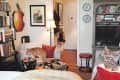 Cozy living room with bookshelves, a cat on a chair, colorful pillows, and framed art on the walls.