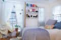 Cozy bedroom with a metal bed, colorful pillows, bookshelves, and a potted plant by a window with sheer curtains.