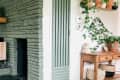 Green stone fireplace with wooden mantel, potted plants, and a wooden side table with woven baskets and decor.