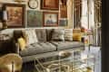 Cozy living room with a tufted gray sofa, eclectic wall art, gold accents, and a glass coffee table.