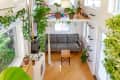 Tiny house interior with a gray sofa, wooden floor, hanging plants, and a loft area with potted plants.