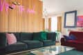 Living room with green and red sofas, neon sign, colorful artwork, and a glass coffee table.