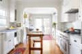 Bright kitchen with white cabinets, wooden island, copper kettle on stove, and red rugs on hardwood floor.