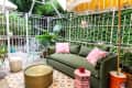 Green outdoor patio with a sofa, pink cushions, round gold table, and striped yellow umbrella.
