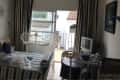 Small bedroom with striped bedding, TV, balcony view, and two white chairs at a round table.