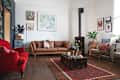 Cozy living room with a brown leather sofa, red armchair, wood stove, and eclectic wall art.