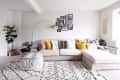 Beige sectional sofa with colorful pillows, geometric rug, gallery wall, floor lamp, and potted plants in a bright living room.