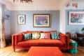 Orange sofa with colorful patterned cushions, framed art on blue walls, and wooden floor in a cozy living room.