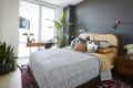 A bedroom with a rattan bed frame, a black focal wall, and floor-to-ceiling windows