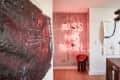 Modern dining area with abstract art, neon "Kiss Me Karl" sign, and geometric chandelier.