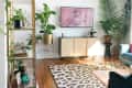Living room with blue velvet sofa, leopard print rug, large plants, and a wall-mounted TV displaying a pink art piece.