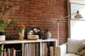 Cozy living room with a white armchair, brick wall, bookshelf, plants, and a floor lamp.