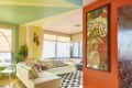 Colorful living room with a white sectional sofa, chevron rug, large windows, and a retro poster on an orange wall.