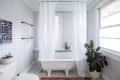 Clawfoot bathtub with white curtain, geometric floor tiles, potted plant, and abstract wall art in a bright bathroom.