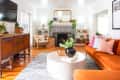 Living room with orange sofa, patterned fireplace, round coffee table, plants, and wooden sideboard.