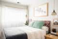 Cozy bedroom with patterned headboard, green pillows, pendant lights, and framed art above the bed.