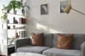 Gray sofa with brown leather pillows next to white bookshelf with plants on top