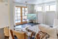 Cozy living room with white sectional sofa, leather chair, TV, and French doors leading to a sunlit patio.