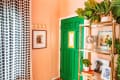 Peach room with green door, polka dot curtains, gold shelf with plants, disco ball, and framed art.