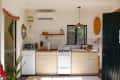 Small kitchen with light wood cabinets, gas stove, microwave, colorful pendant light, and open door to a bathroom.