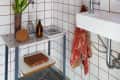Bathroom with red grid tiles, round mirror, small window, white sink, plant, and toiletries on a marble shelf.
