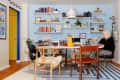 Home office with a round table, colorful bookshelves, striped rug, and a person working on a laptop.