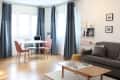 Living room with gray sofa, wooden coffee table, dining area with pastel chairs, and blue curtains.