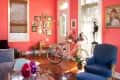 Living room with coral walls, blue armchair, pink bicycle, and eclectic wall art.
