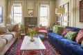 Living room with blue and beige sofas, colorful cushions, marble coffee table, tulips, and a red patterned rug.