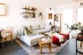 Cozy living room with a light gray sectional, red velvet ottomans, wooden coffee table, and decorative wall shelves.