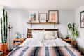 Bohemian bedroom with wooden bed, patterned blanket, cactus, plants, and framed art on a shelf.