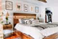 Brass sconces on either side of a large bed with a rustic wood bed frame, with art prints above the bed