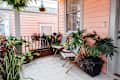 Small porch with pink siding, patterned chairs, and various potted plants.