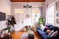 Cozy living room with blue sofa, colorful cushions, potted plants, shoe rack, and wall-mounted TV.