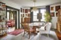Dining room with round table, wooden chairs, chandelier, art-filled walls, and a large plant by the window.