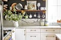 Kitchen with marble countertops, blue stove, hanging mugs, glassware, and a vase with greenery on a shelf.
