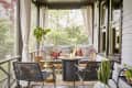 Cozy screened porch with wicker chairs, patterned cushions, fire pit, and potted plants.