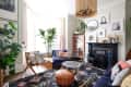 Cozy living room with navy sofas, patterned rug, plants, and eclectic decor around a black fireplace.