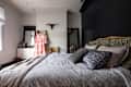 Bedroom with a striped bedspread, floral pillows, black accent wall, and a dress hanging near a mirror and dresser.