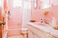 Pink bathroom with tiled walls, pink bathtub, matching sink, white shower curtain, and yellow flowers on the counter.