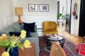 Living room with gray sofa, yellow velvet chair, red cushioned chair, and a round glass coffee table on a patterned rug.