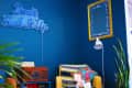 Cozy room with blue walls, neon sign, yellow armchair, colorful pillows, and a vintage radio.