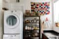Laundry room with stacked washer and dryer, wooden shelves with jars, plants, and a colorful patchwork wall hanging.