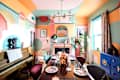 Colorful dining room with abstract wall art, a piano, eclectic decor, and a table set with unique plates and a copper vase.