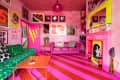 Vibrant living room with pink walls, striped floor, green sofa, pink couch, colorful art, and a bright pink fireplace.