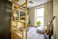 Home office with a desk, ergonomic chair, bookshelves, guitar, plants, and a large window.